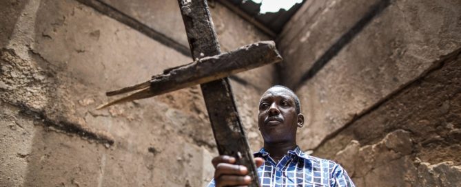 Man holding a wooden cross overhead near a stone wall - prophecy second coming